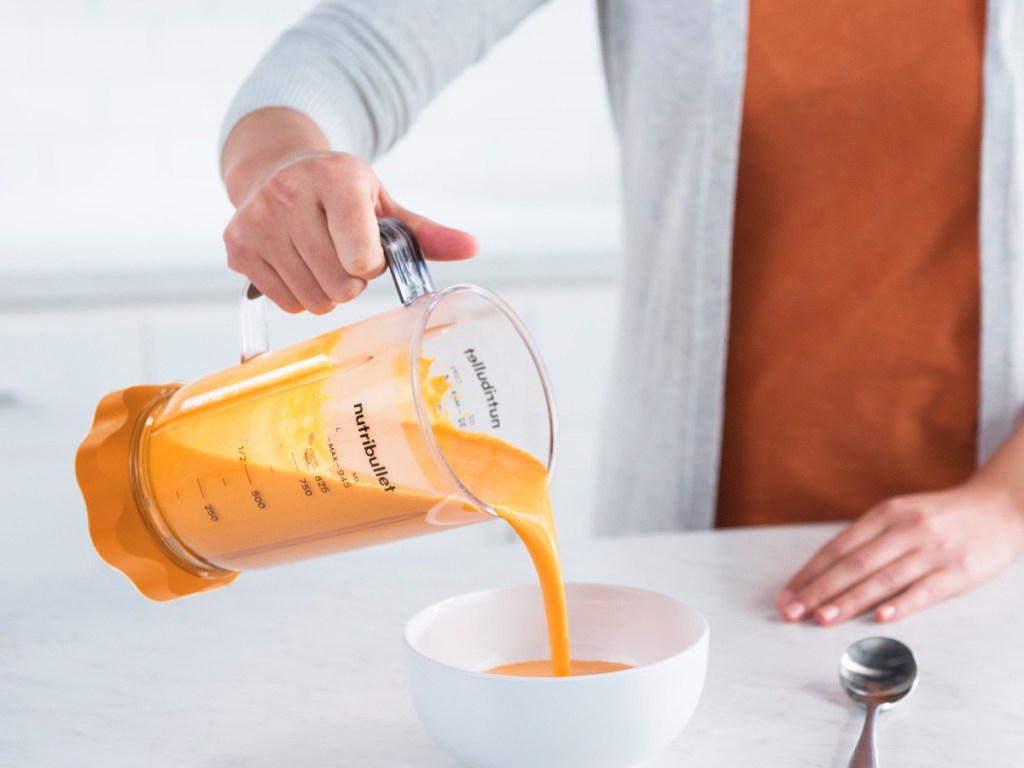 woman pouring orange liquid from a nutribullet blender