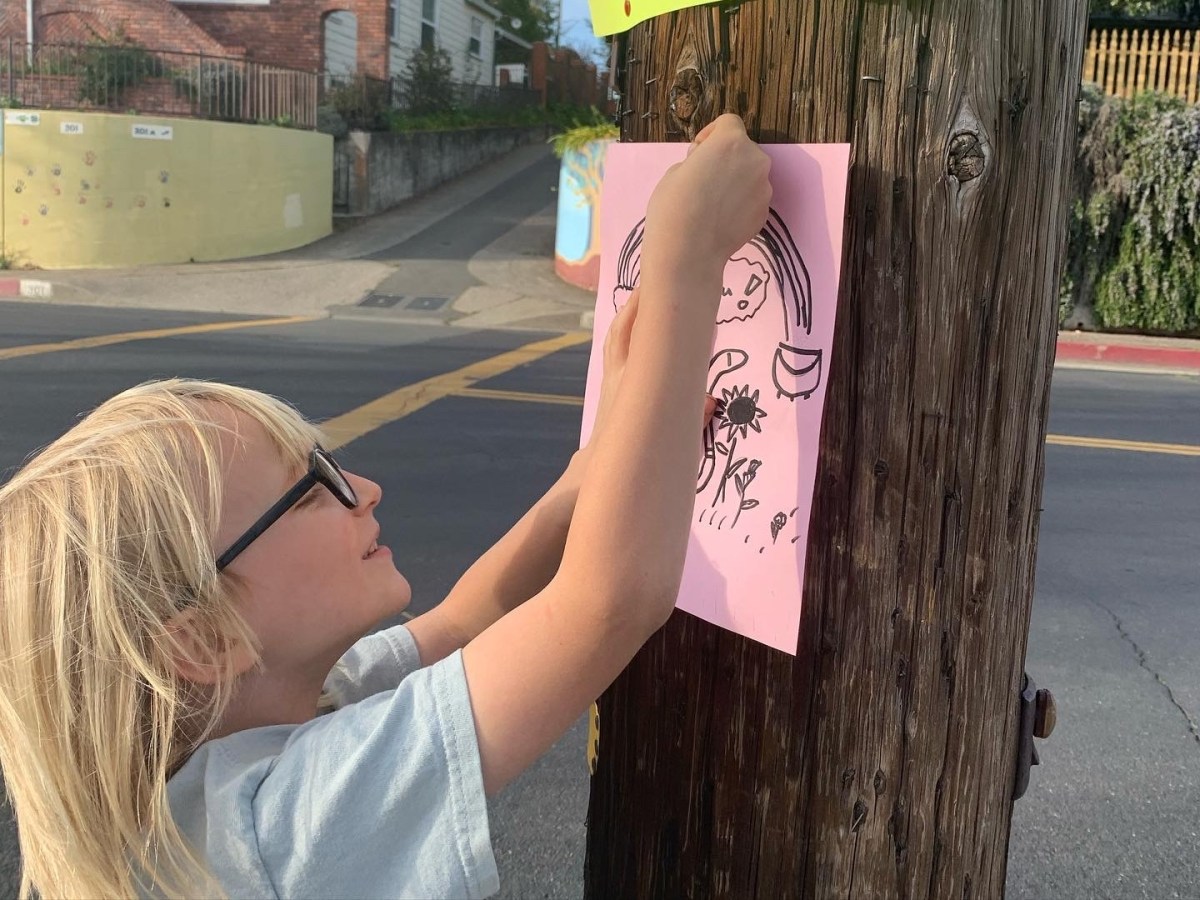 girl hanging pink sign on utility pole