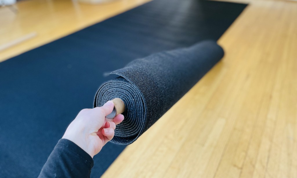 hand holding a roll of black padding over wood floor