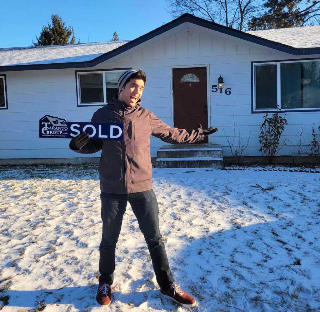 man holding sold sign in front of house with snow on ground