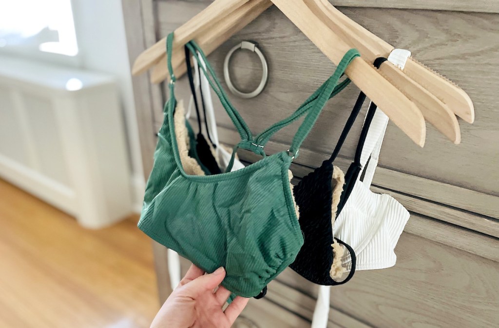 hand holding green bathing suit top hanging from wood hanger on dresser