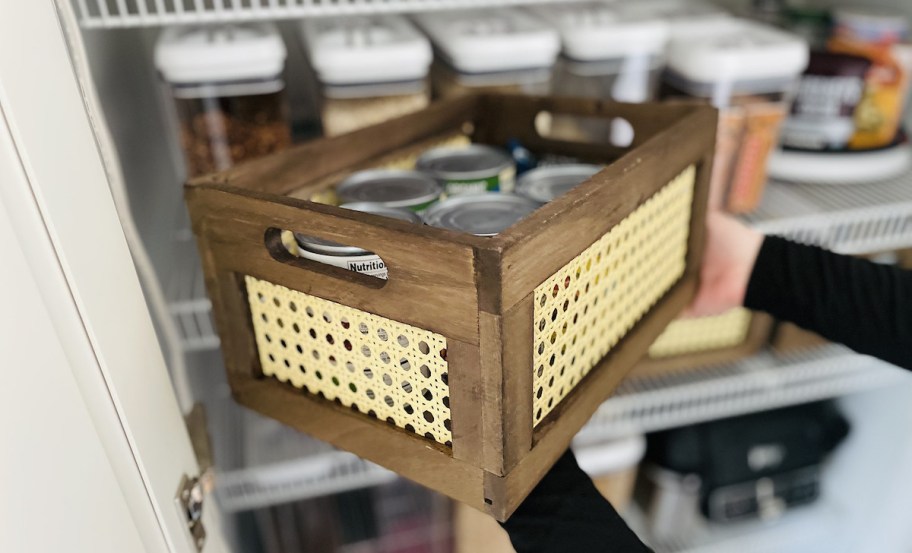 hands holding brown rattan and wood crate with cans inside