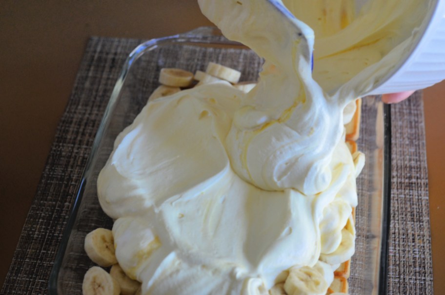 Pouring banana pudding into a baking dish lines in order to show how to make banana pudding with chessmen cookies
