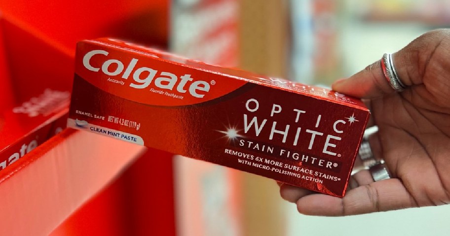 hand pulling Colgate Optic White Toothpaste off shelf