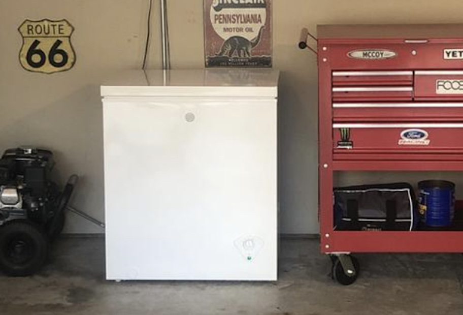 Small white chest freezer on garage floor next to red toolbox