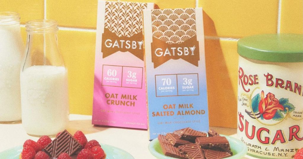 two Gatsby chocolate bars leaning up against a tile wall surrounded by plates of chocolate squares, strawberries, a sugar canister and a glass of milk
