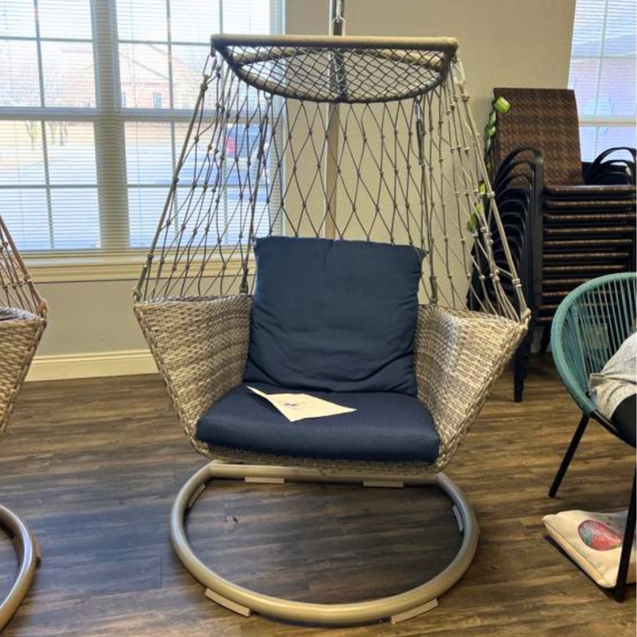 tan color hanging chair with wicker and rope on a steel frame with a blue cushion