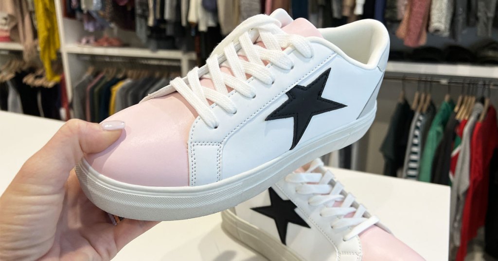hand holding up white and pink sneaker with black star