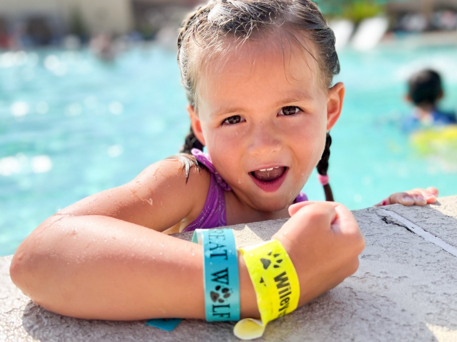 Kid with wrist bands sitting leaning on edge of the pool