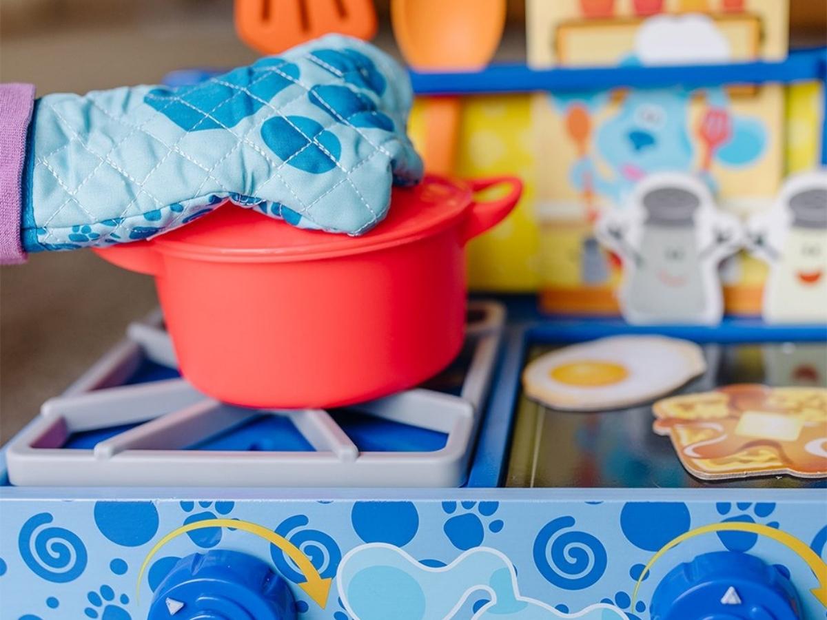 child wearing a toy oven mit and lifting the lid of a pot from the Melissa Doug Blues Clues Cooking Play Set