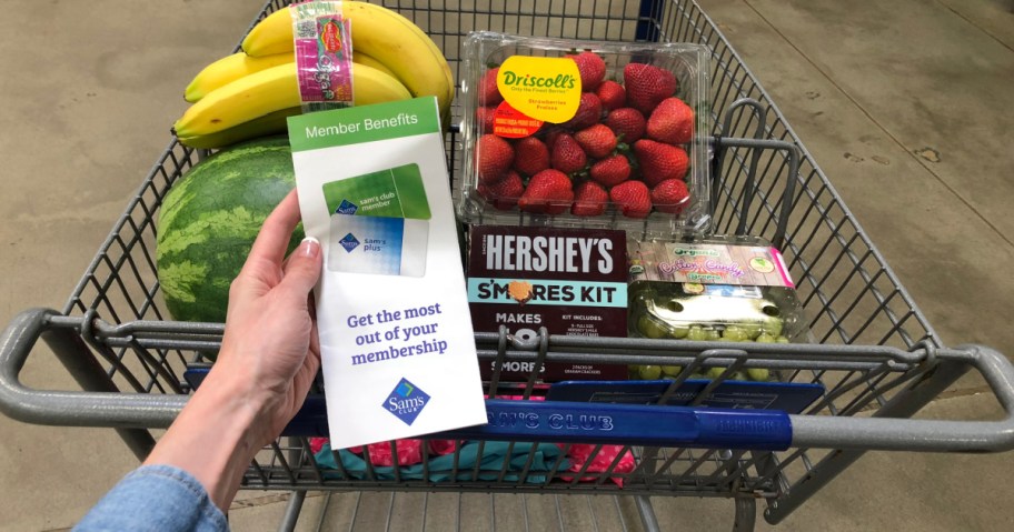 woman holding Sam's Club Brochure in front of shopping cart filled with food