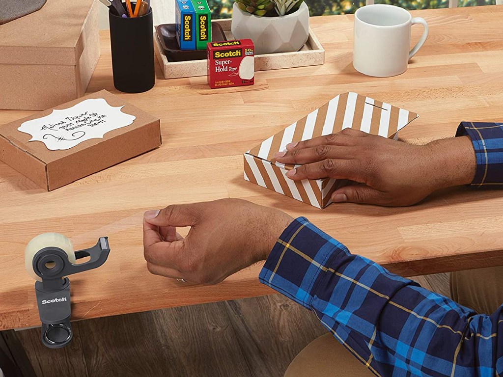 man's hand pulling tape of tape dispenser to wrap present