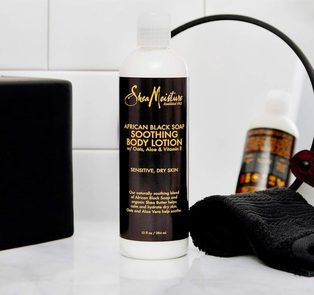 SheaMoisture Soothing African Black Soap Lotion for Troubled Skin in front of a small round mirror and next to a black washcloth