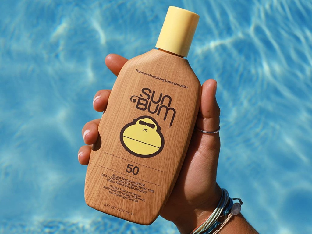 hand holding bottle of sunscreen over pool