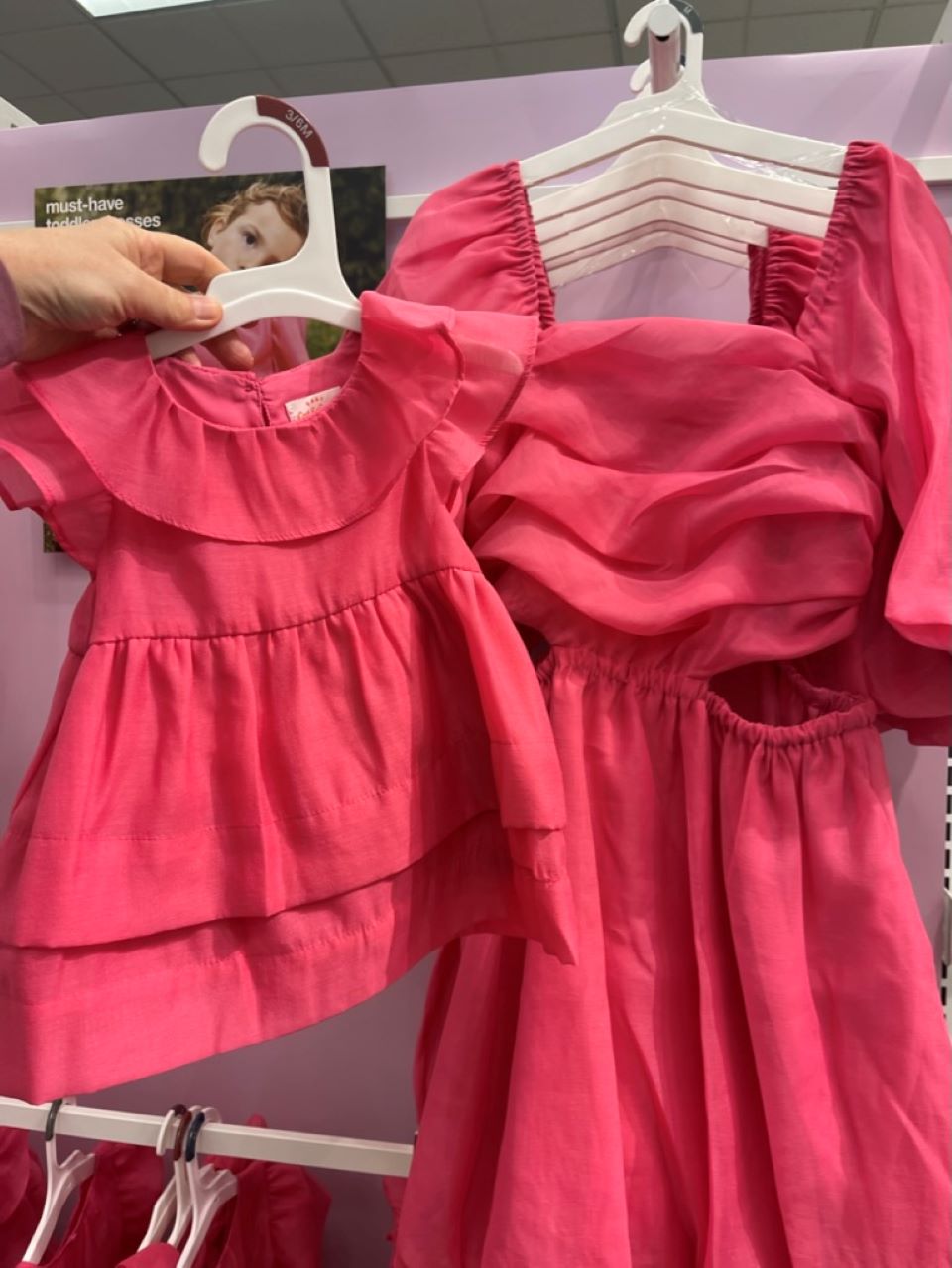Hand holding a dress on a pink hanger next to another dress on a hanger