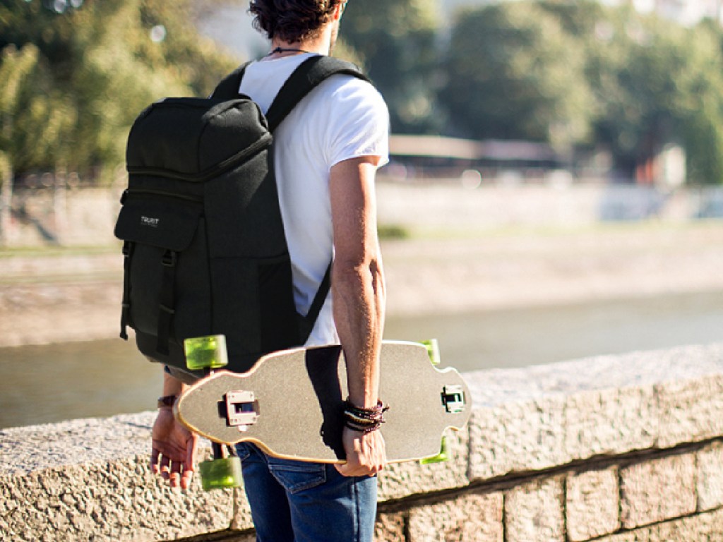 man wearing black backpack walking with skateboard