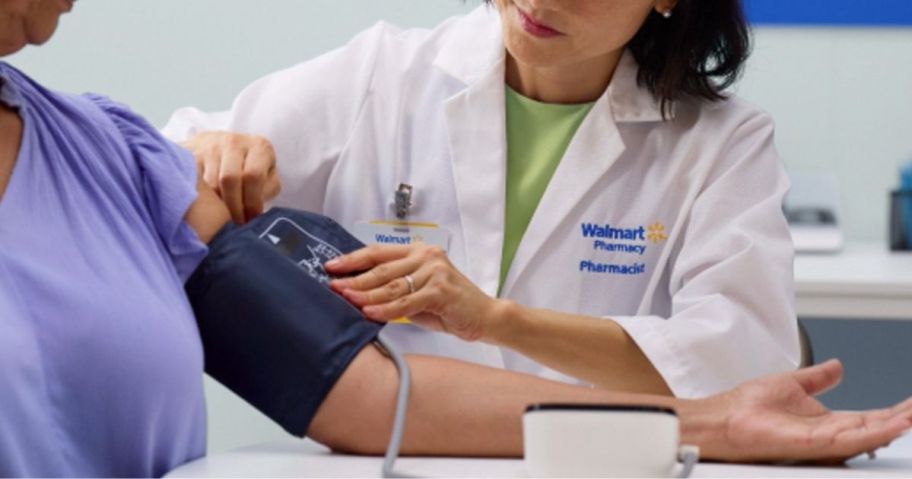 A woman wearing a Walmart pharmacist's coat is taking the blood pressure of another woman
