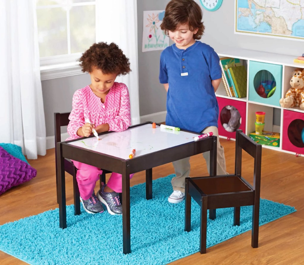 girl drawing on a dry erase table with a boy watching her