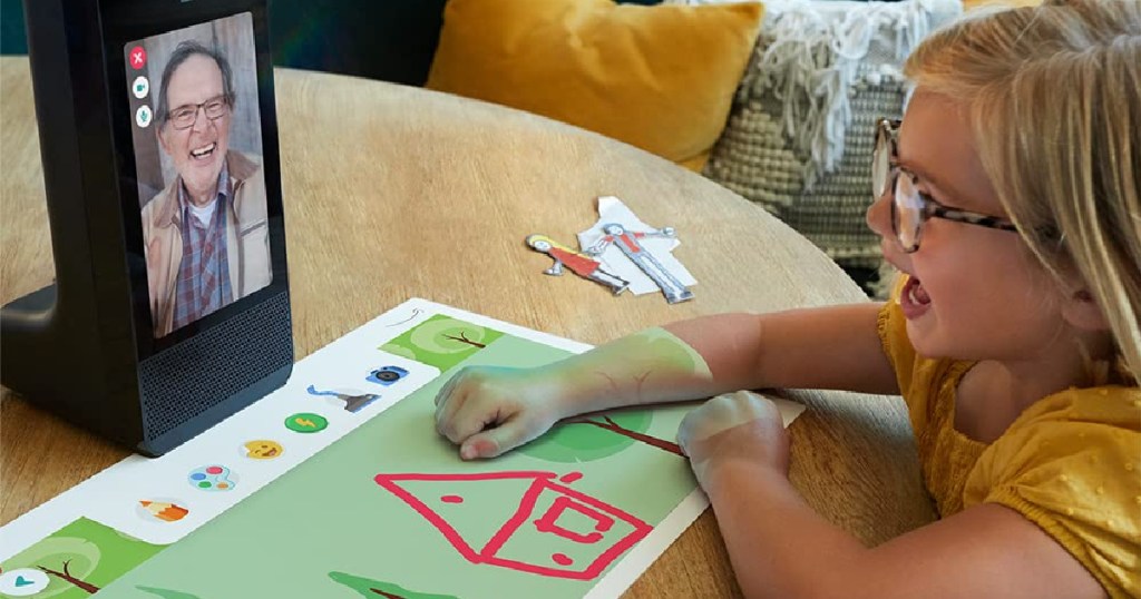 girl coloring on a mat while a loved one watches via video chat