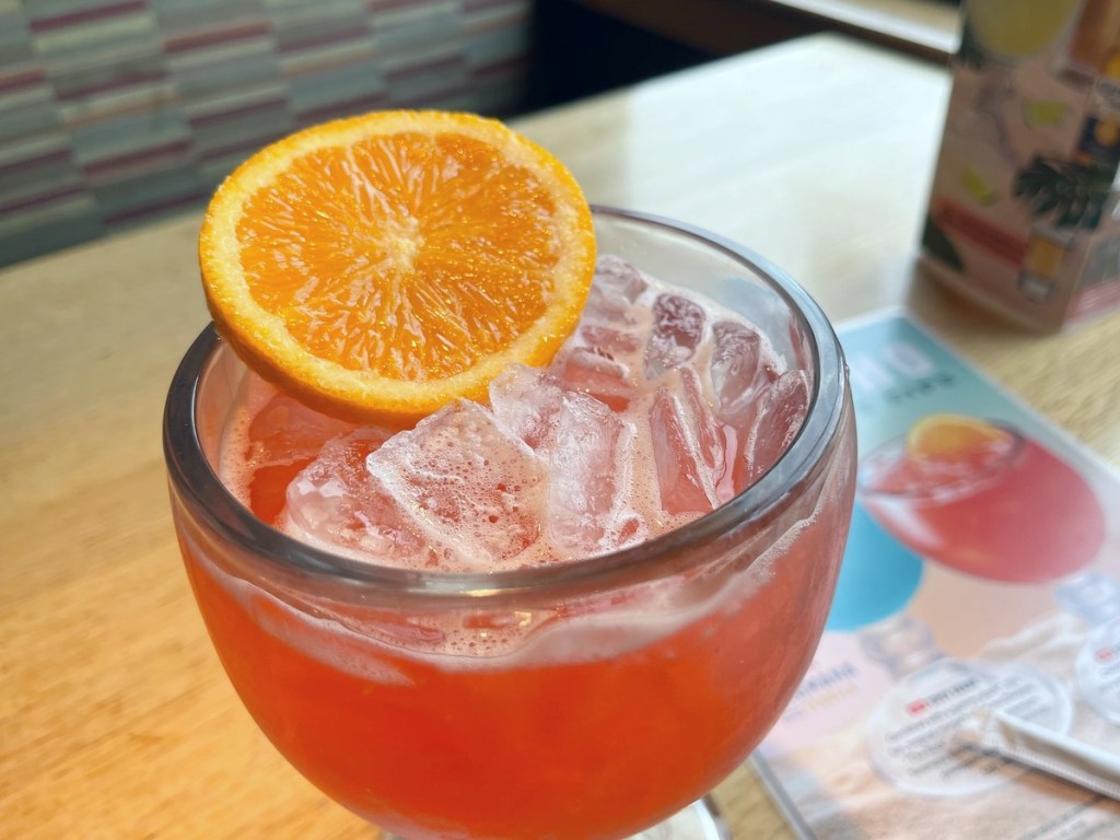 red cocktail garnished with an orange slice