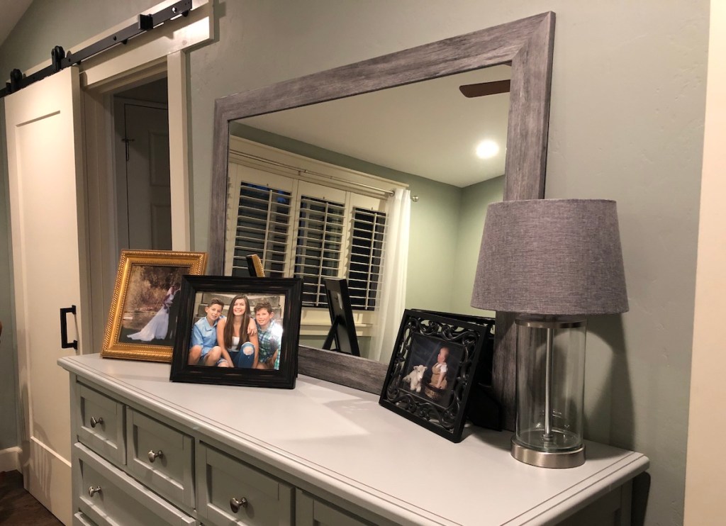 wood frame mirror on console table with picture frames and lamp