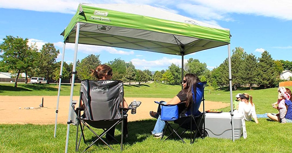 green and white coleman canopy tent in park with two women sitting under it in chairs