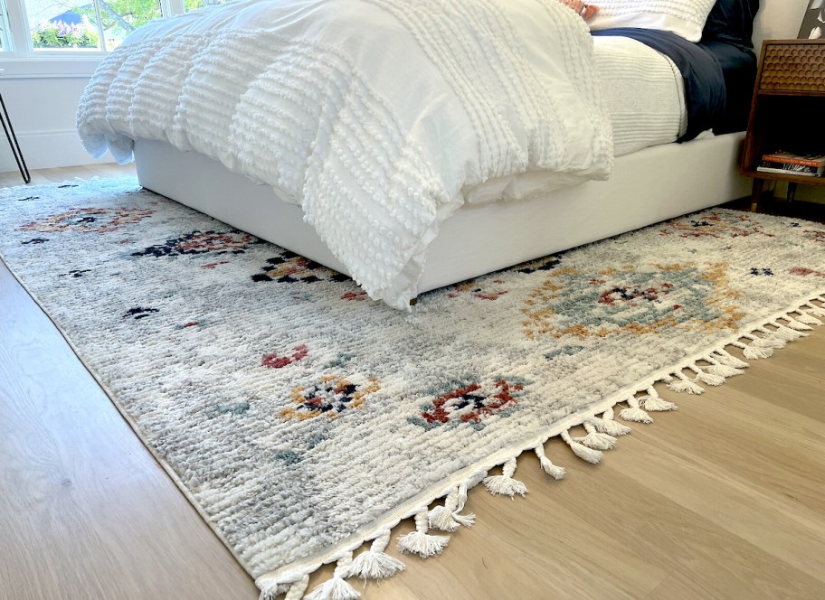 southwestern rug with tassels on floor with white bed and accent chair in corner