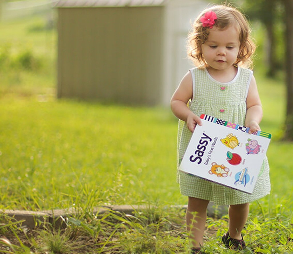 toddler girl walking in grass holding book