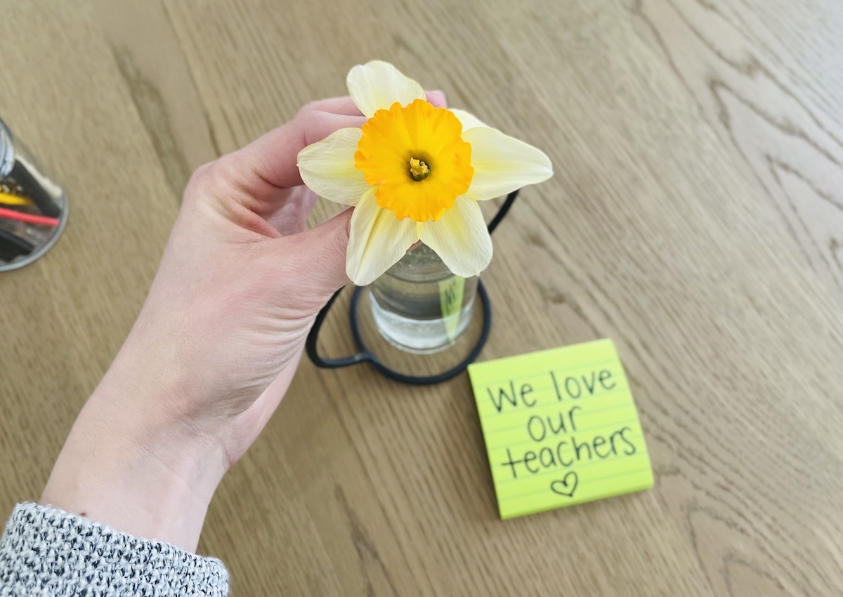 hand holding a yellow and orange flower with we love our teachers post it note as a teacher appreciation gift