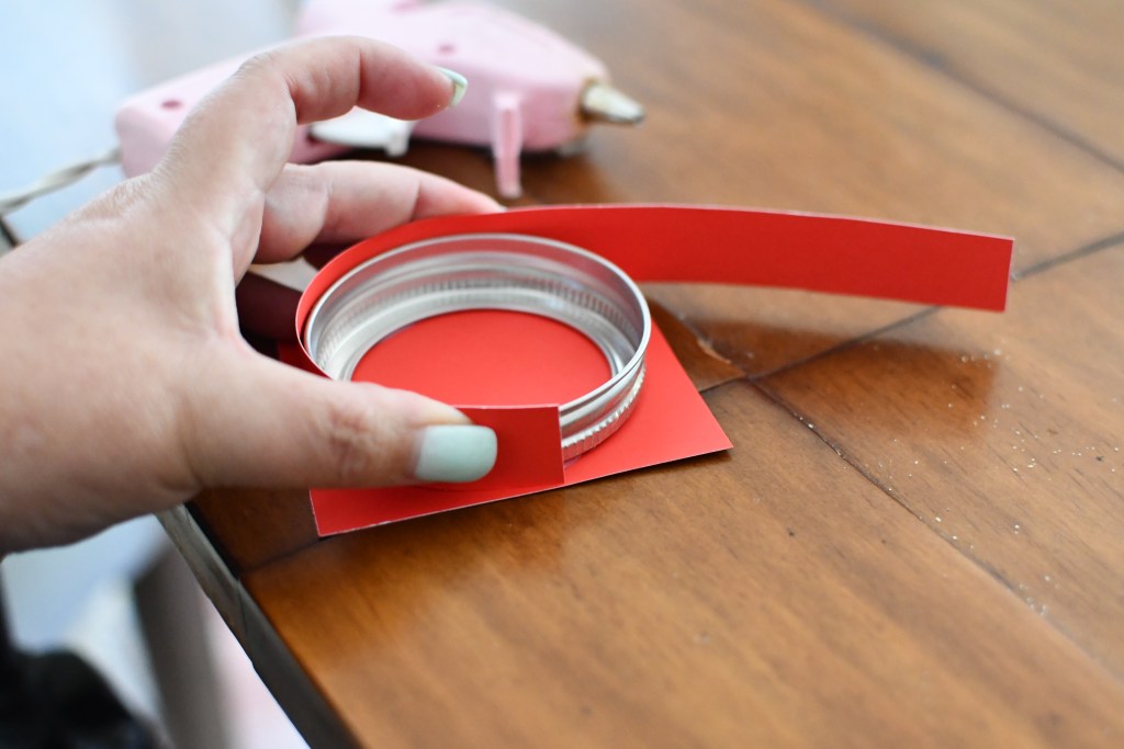 gluing red square and paper to lid of a jar