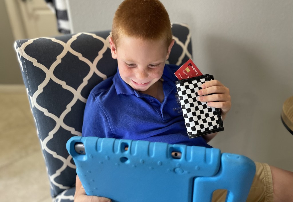 boy sitting on chair with ipad holding black and white checked wallet