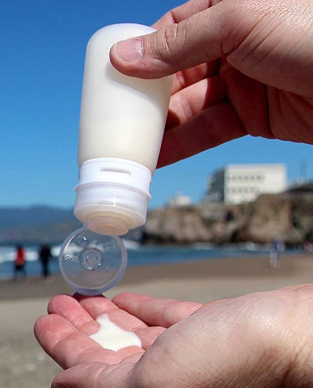 hand squeezing silicone tube of lotion on beach