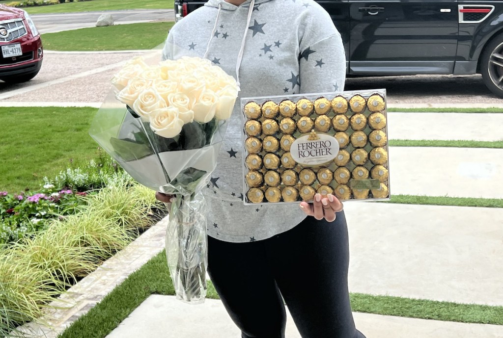 woman holding white roses and box of chocolates standing on walkway