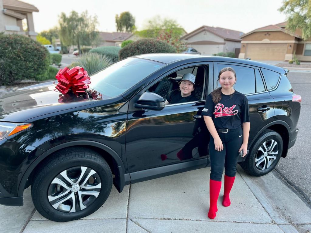 teen sitting in black honda with big red bow on driveway