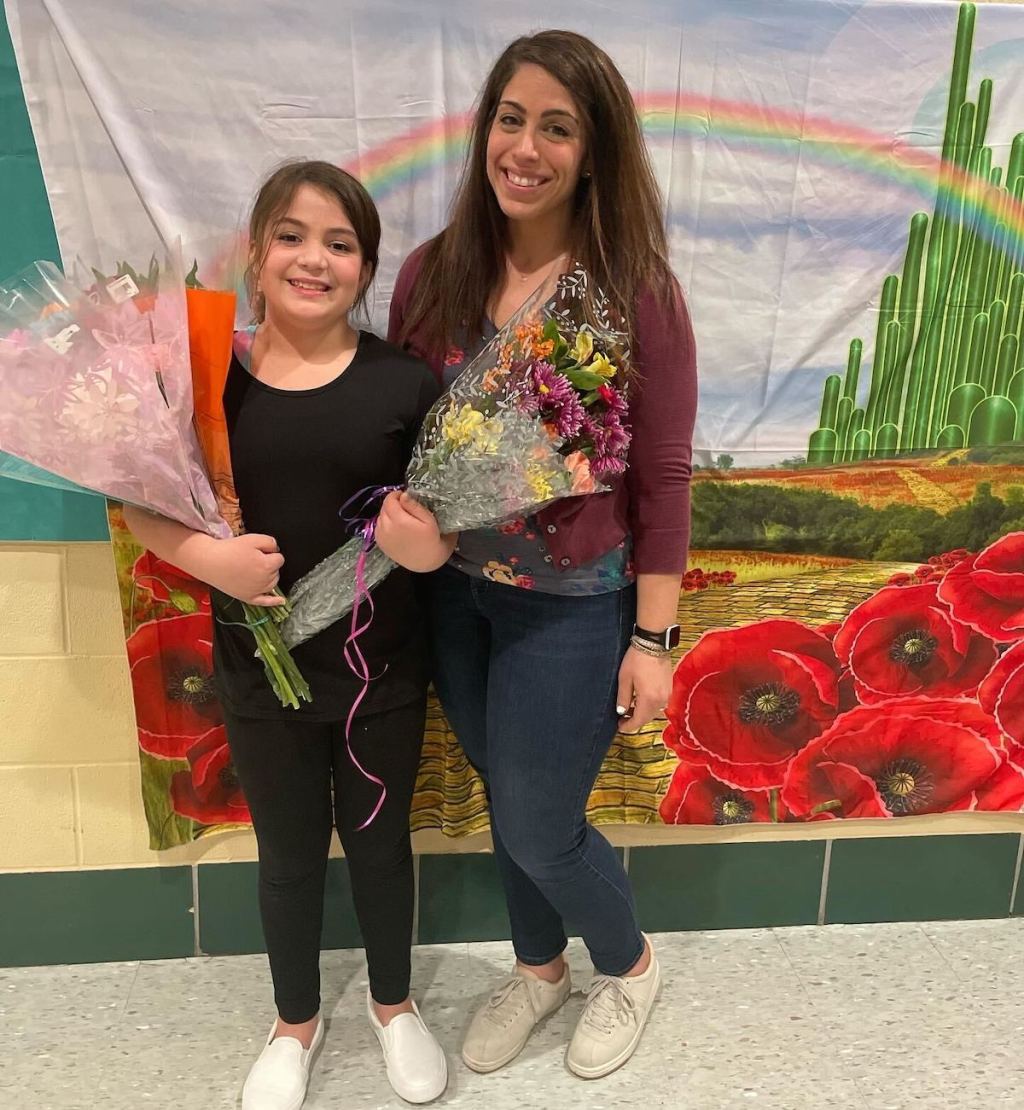 mom and daughter holding flowers smiling in front of rainbow tapestry