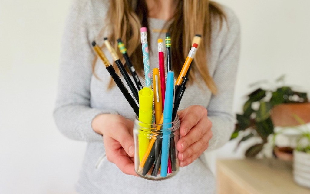 woman holding clear jar of pens and pencils