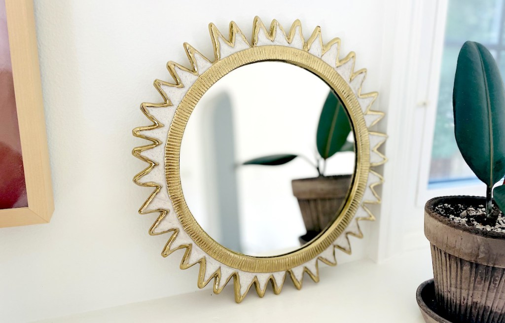 round gold starburst mirror leaning on white wall next to plant