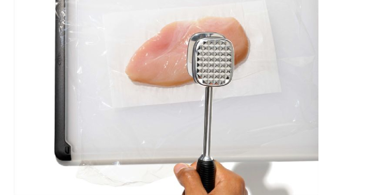 hand using a meat tenderizer on chicken