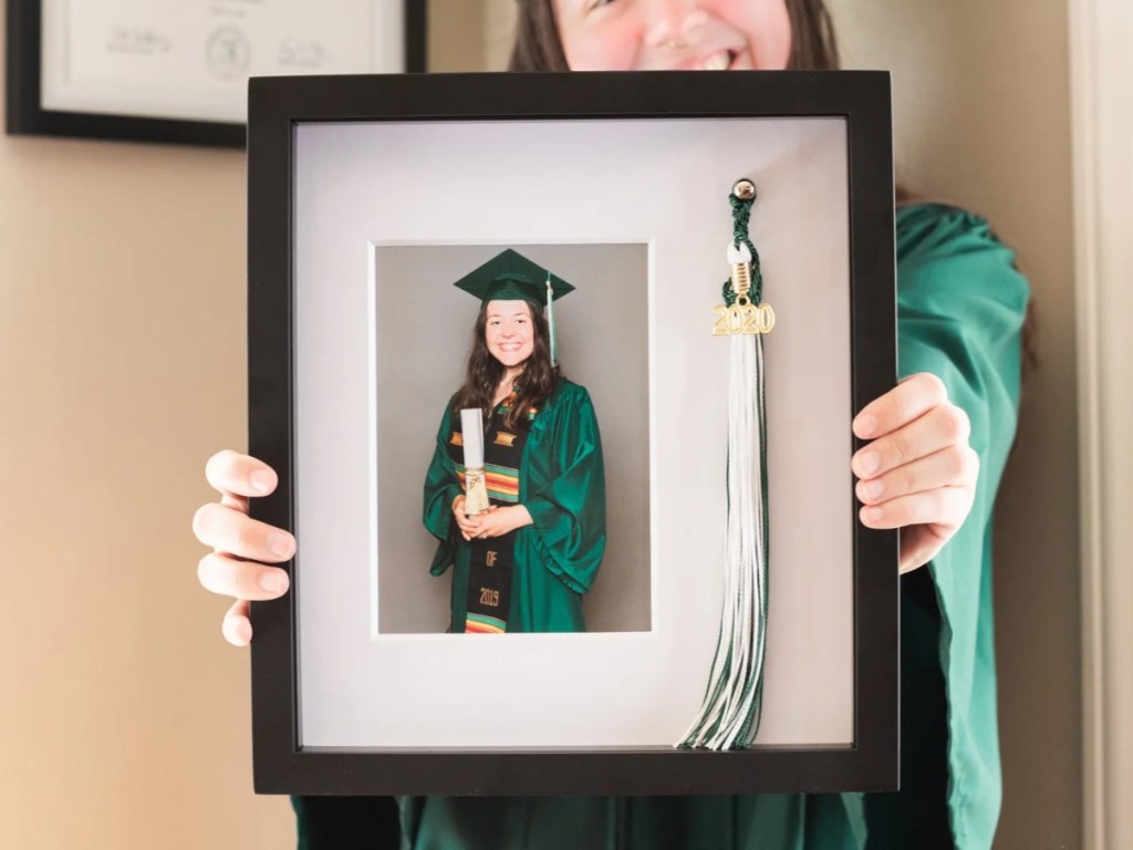 holding a framed graduation photo and tassel 