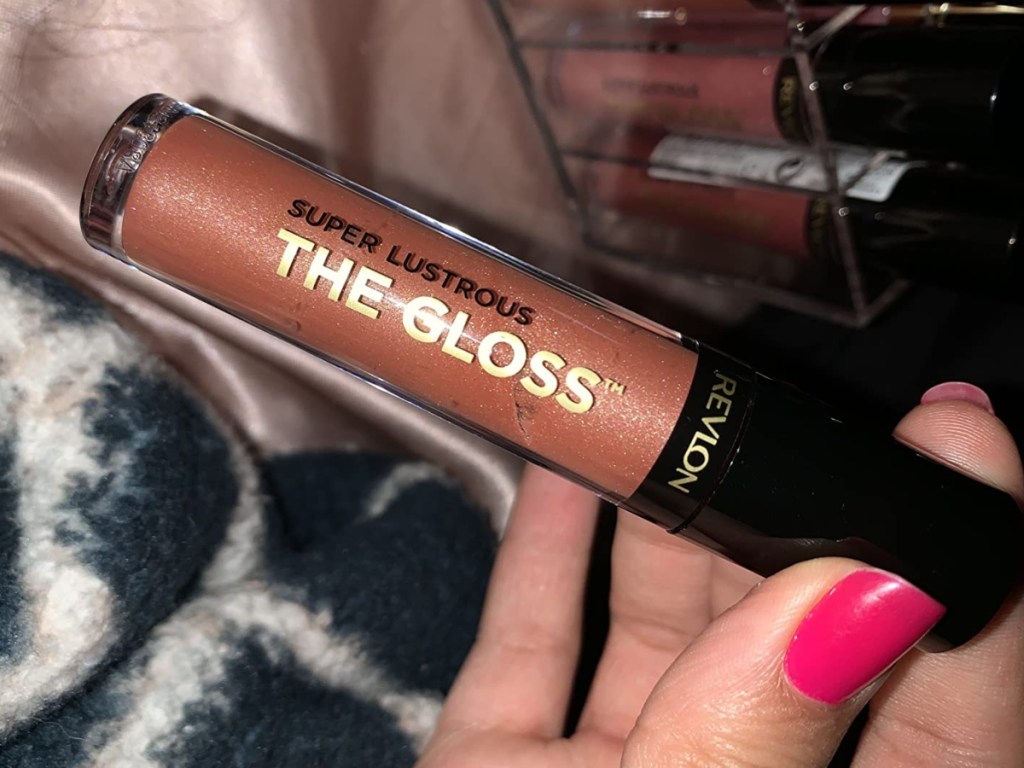 holding a tube of shimmery nude lip gloss