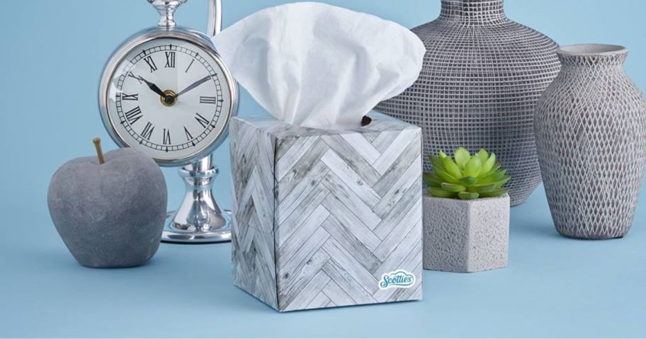 scotties tissue box with tissue coming out on blue table with clock, and vases