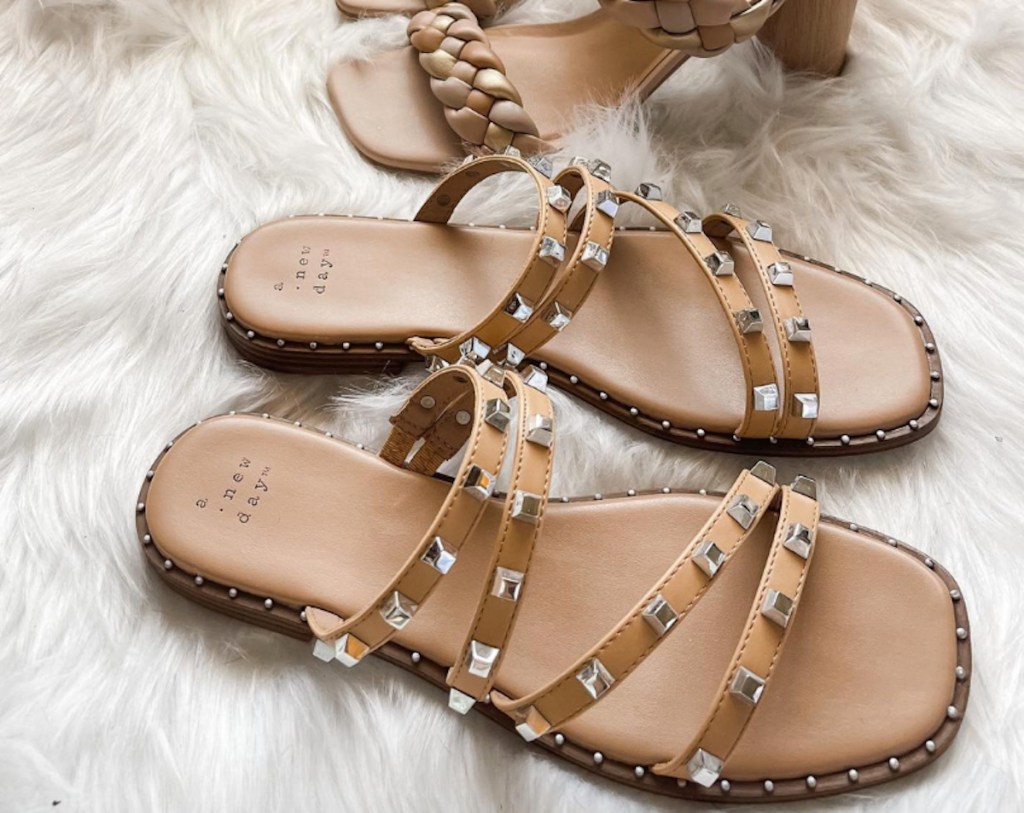 close up of tan studded sandals sitting on white faux fur rug