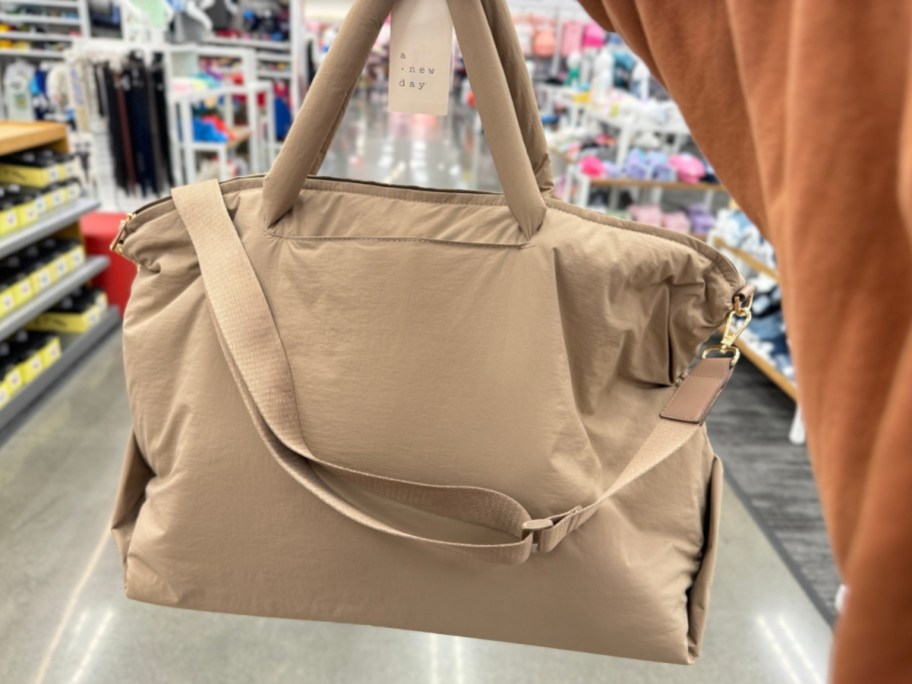 person holding up a brown/tan puffy weekender bag in a store