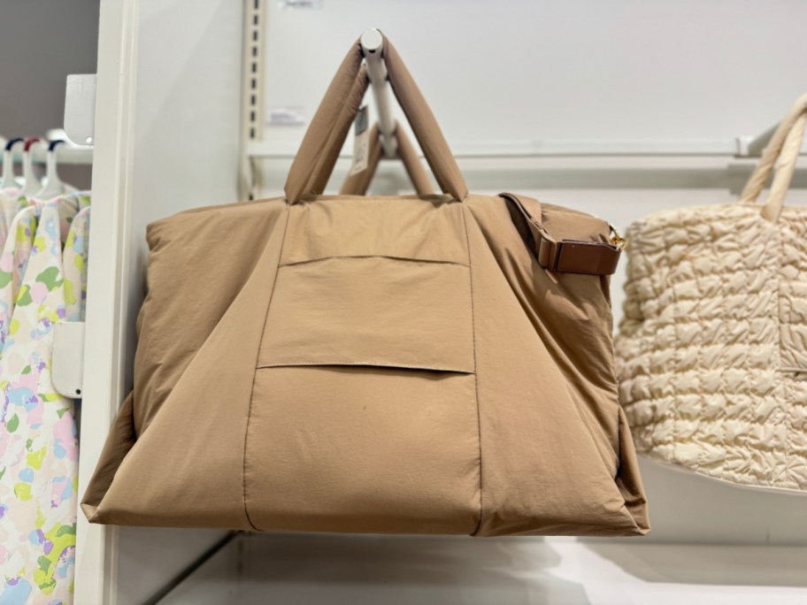 brown/tan puffy weekender bag hanging from a wall display in store