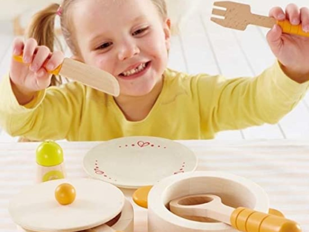 Child playing with wooden kitchen accessories on counter