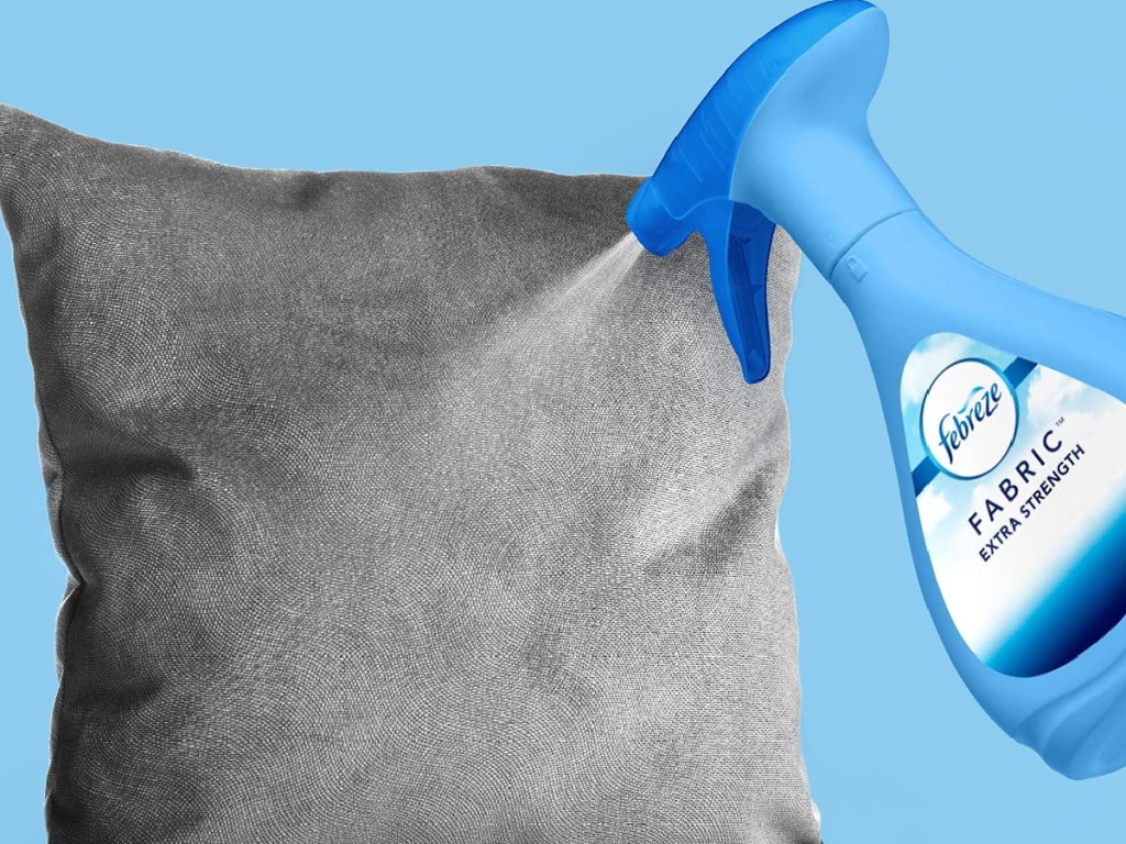 Febreze Fabric Spray being sprayed onto blue/gray throw pillow