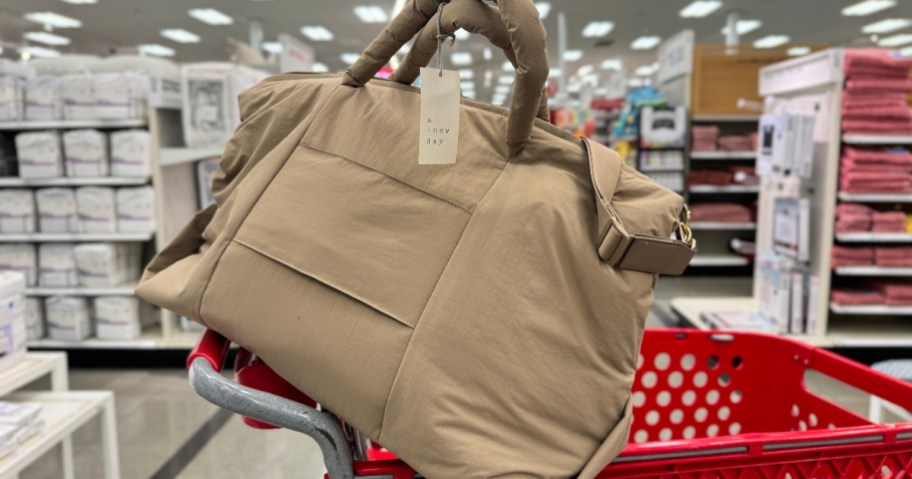 brown / tan color puff weekender bag with handles sitting on top of a Target cart