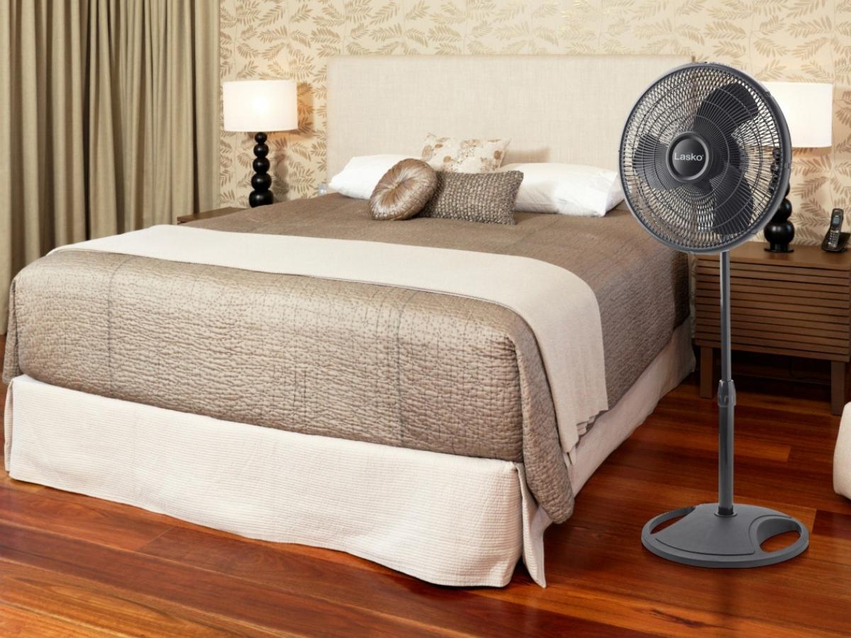 bed covered in white and pewter linens with a black pedestal fan on the floor next to it