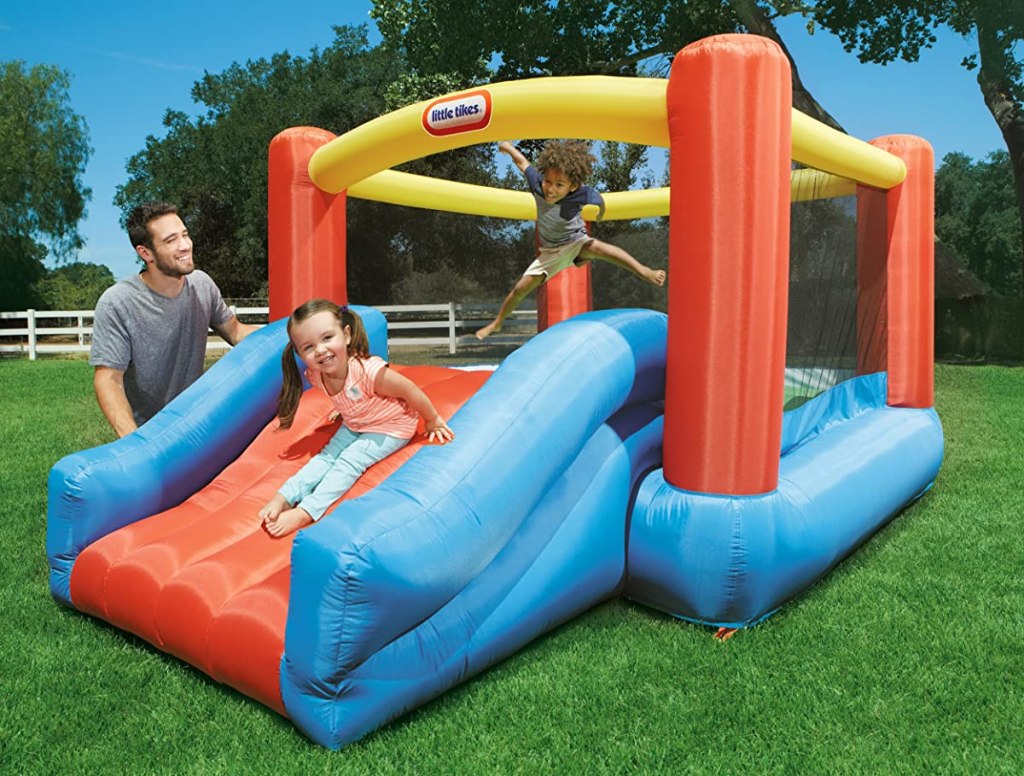 two kids playing on a Little Tikes bounce house Jr. Jump 'n Slide Bouncer with a man standing nearby