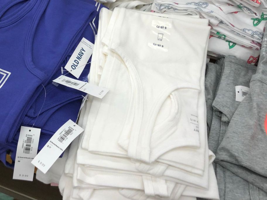 A stack of folded girls white tank tops on a display at Old Navy